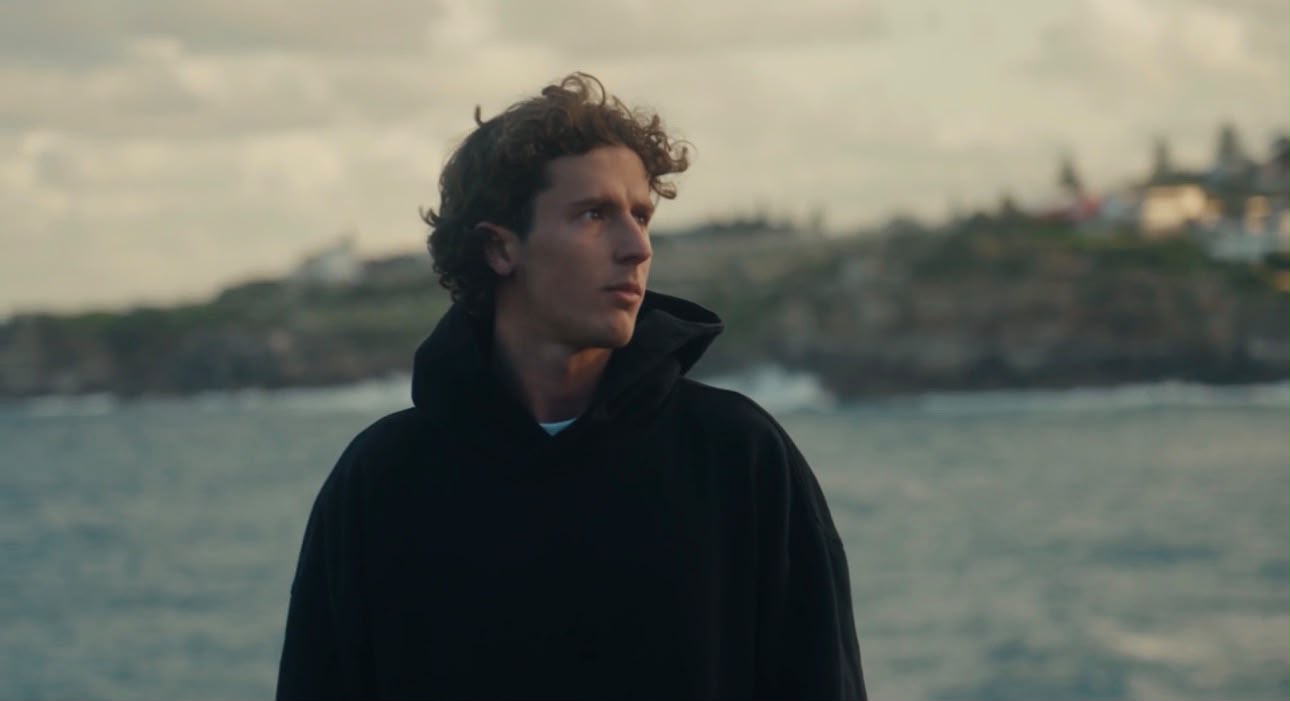 Marcel in a black hoodie on the coast, looking off to the side.